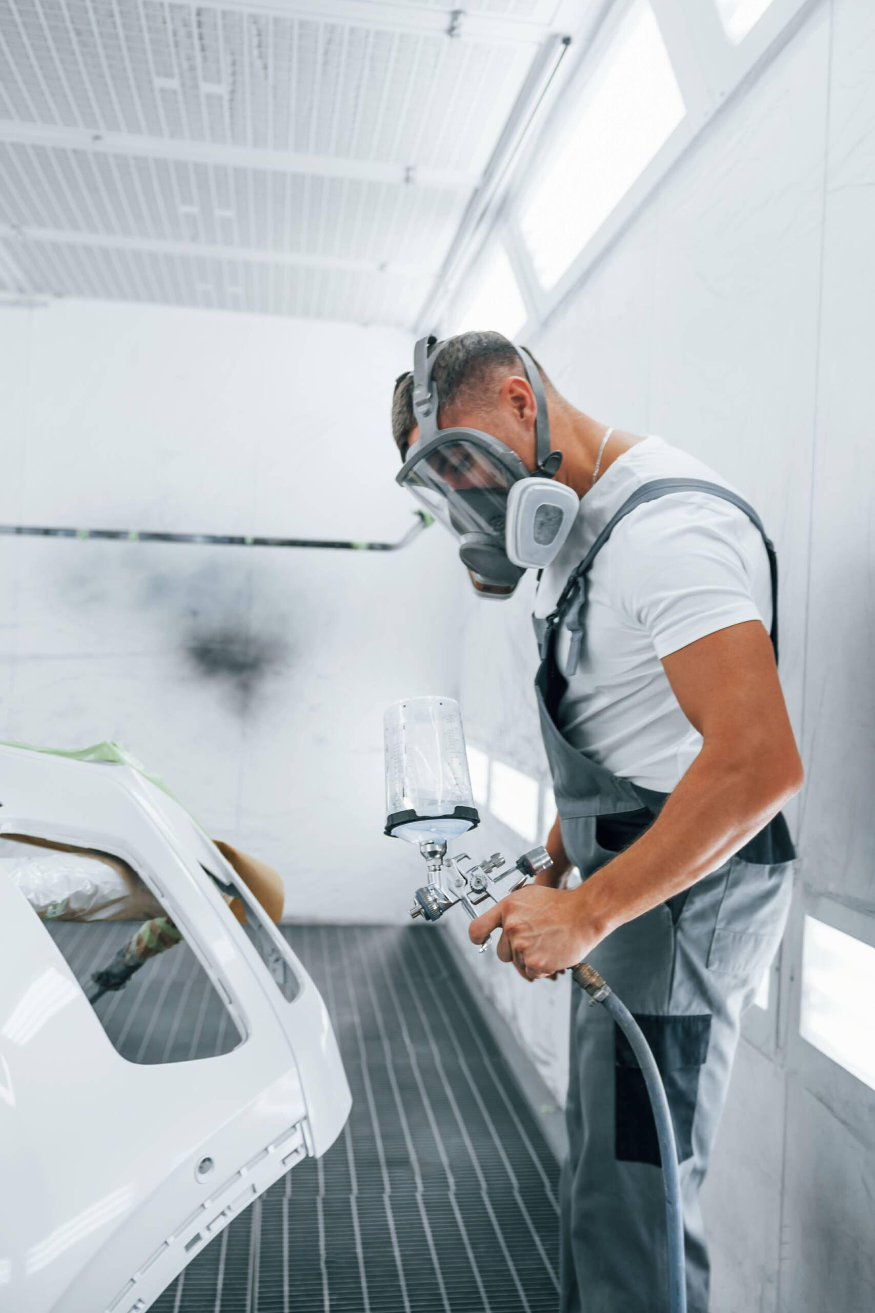 Con pistola de pintura. Un mecánico caucásico, uniformado, trabaja en un taller.